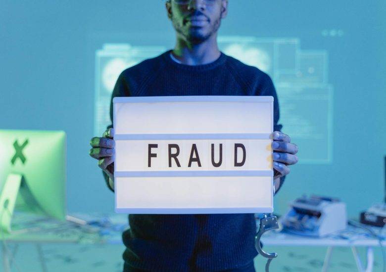 a man in black sweater holding letter board with fraud text